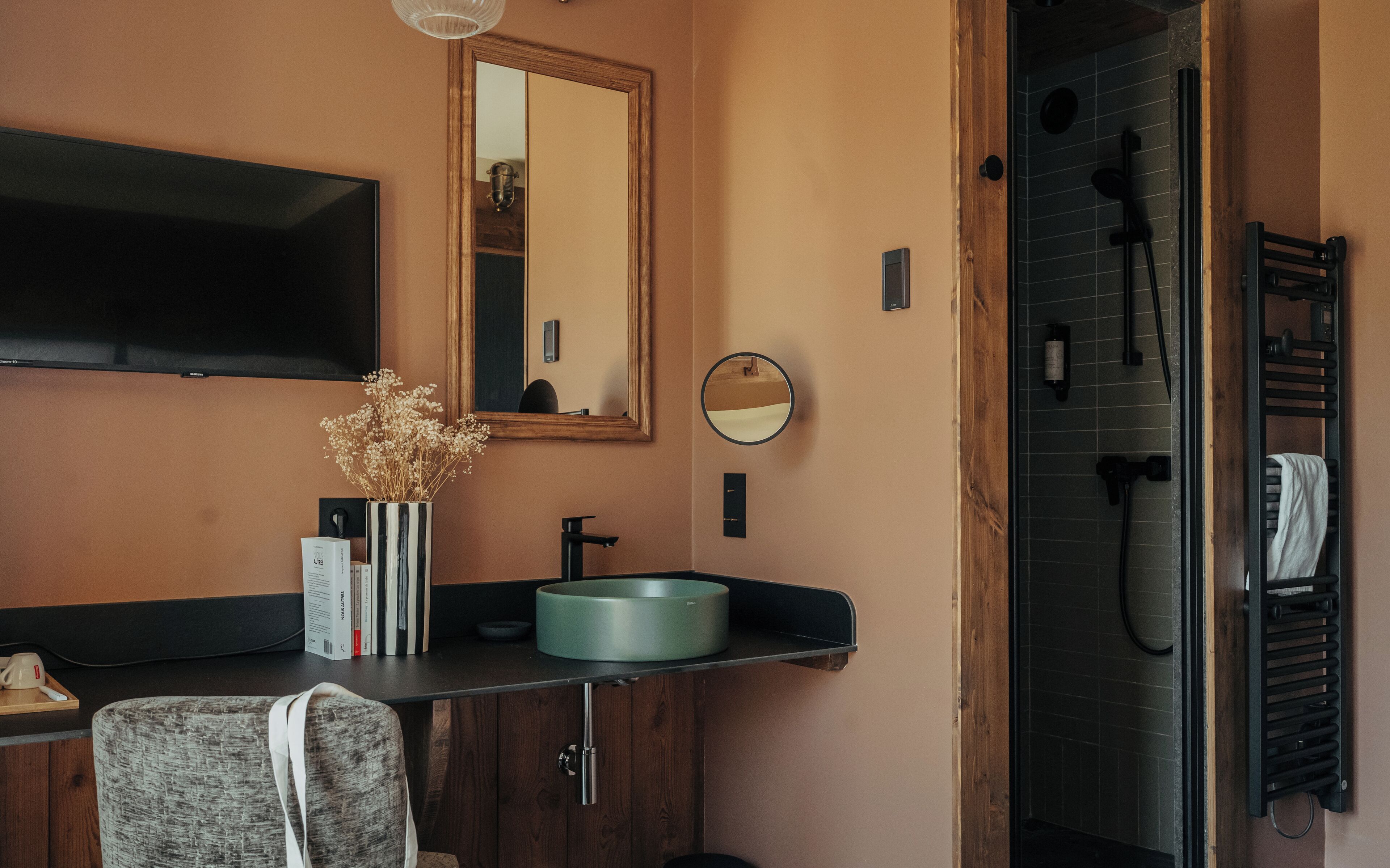 Un baño moderno con tocador de madera, espejo redondo, lavabo empotrado y zona de ducha.