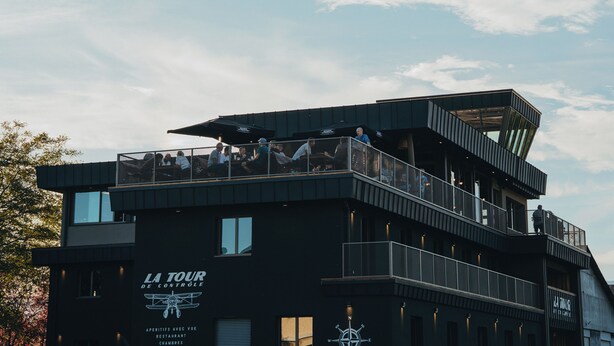 A modern building with a sign reading "LA TOUR DE CONTROLE" and a restaurant named "RESTAURANT CHAMBRES".