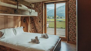 A bedroom with a bunk bed, a large window with a view of a green landscape and a plane, and floral wallpaper.