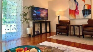 Una sala de estar con una televisión, un cuadro abstracto grande, dos sillones de cuero, una lámpara de pie y una planta en maceta.