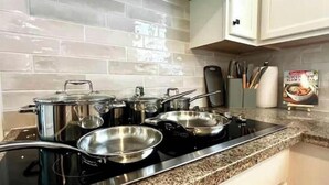 Una cocina con estufa negra, ollas de acero inoxidable y encimera de granito.