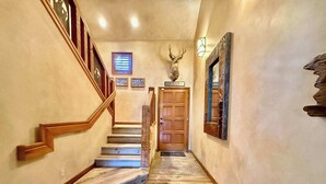 Un escalier en bois, avec une tête de cerf fixée au-dessus de la porte.
