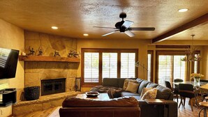 Un salon spacieux doté d’une cheminée, d’un ventilateur de plafond et d’une grande fenêtre laissant entrer la lumière naturelle.