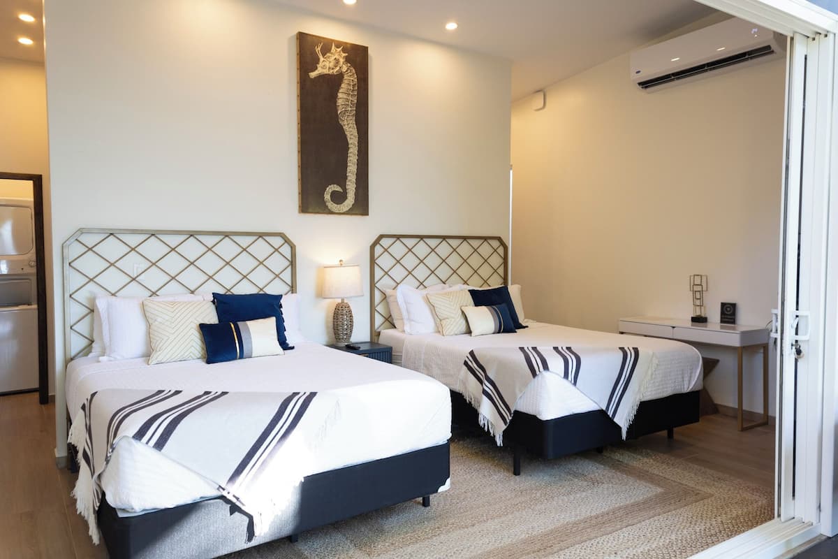 A hotel room with two beds, a seahorse artwork, a desk, and a door.