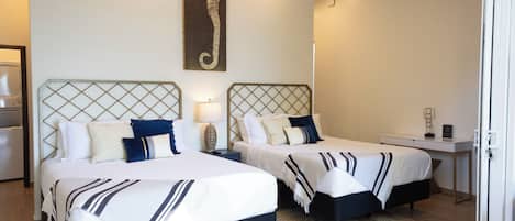 Ein Hotelzimmer mit zwei Betten, einem Kunstwerk mit einem Seepferdchen, einem Schreibtisch und einer Tür.