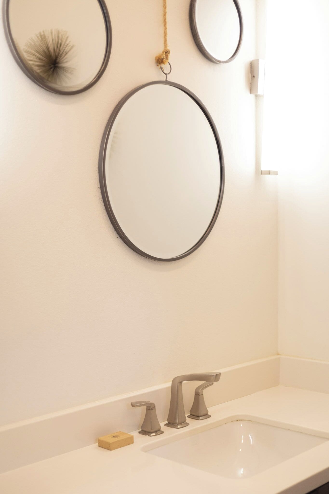 A bathroom with a large mirror, two smaller mirrors, a sink with two faucets, and a soap dish.