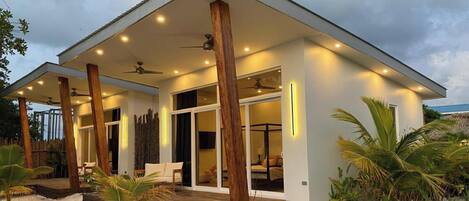 Una casa moderna frente a la playa con un porche cubierto, ventanas amplias y una terraza de madera.