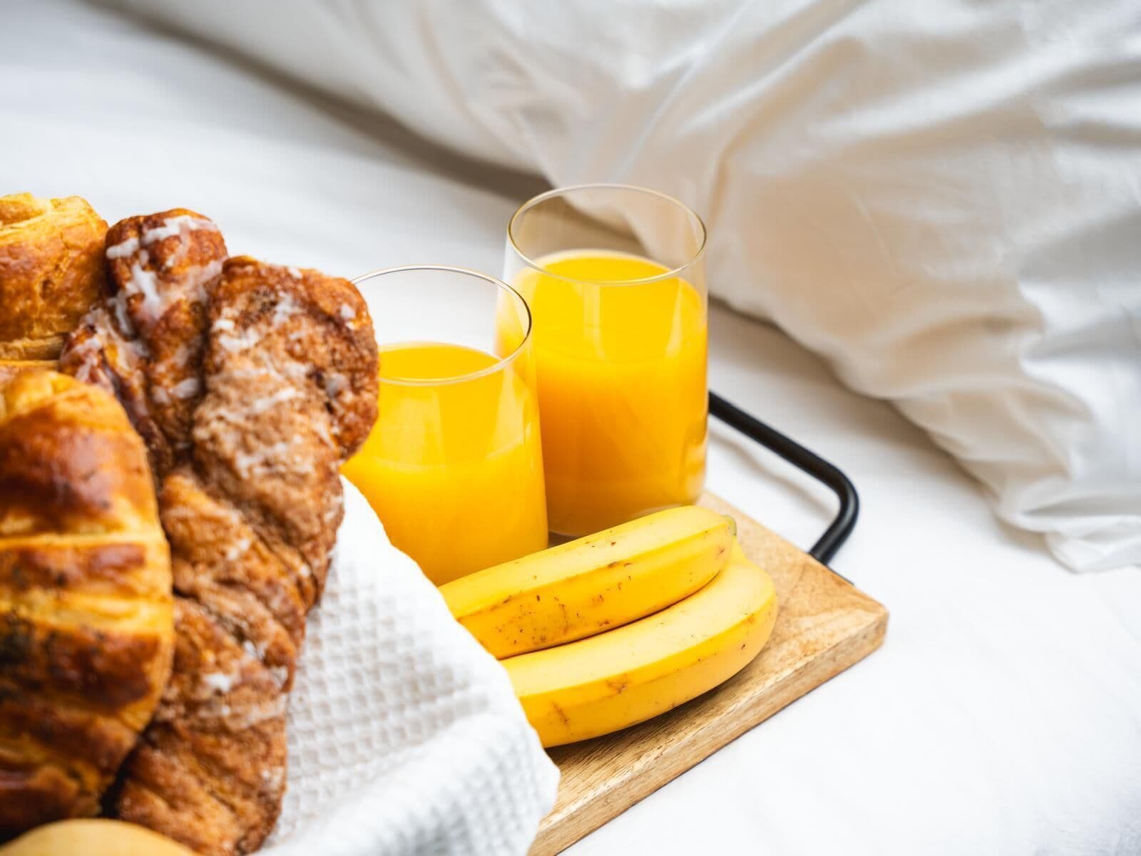 Desayuno con pan, plátanos y jugo de naranja sobre una tabla de madera.