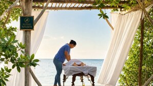 A wooden deck with a massage table and a person attending to a client, overlooking a body of water. - The Bohemian Caye Caulker (Caye Caulker)