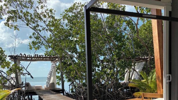 A bedroom with a large window, a bed, and a view of the beach. - The Bohemian Caye Caulker (Caye Caulker)