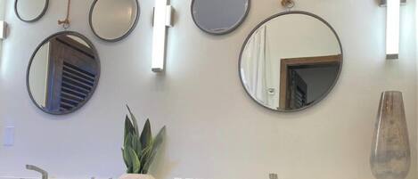 Un baño con varios espejos redondos, una planta en maceta y un florero en el tocador.