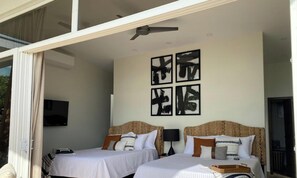 Ein Hotelzimmer mit zwei Betten, einem Deckenventilator, Bildern an der Wand und einem an der Wand befestigten Fernseher.