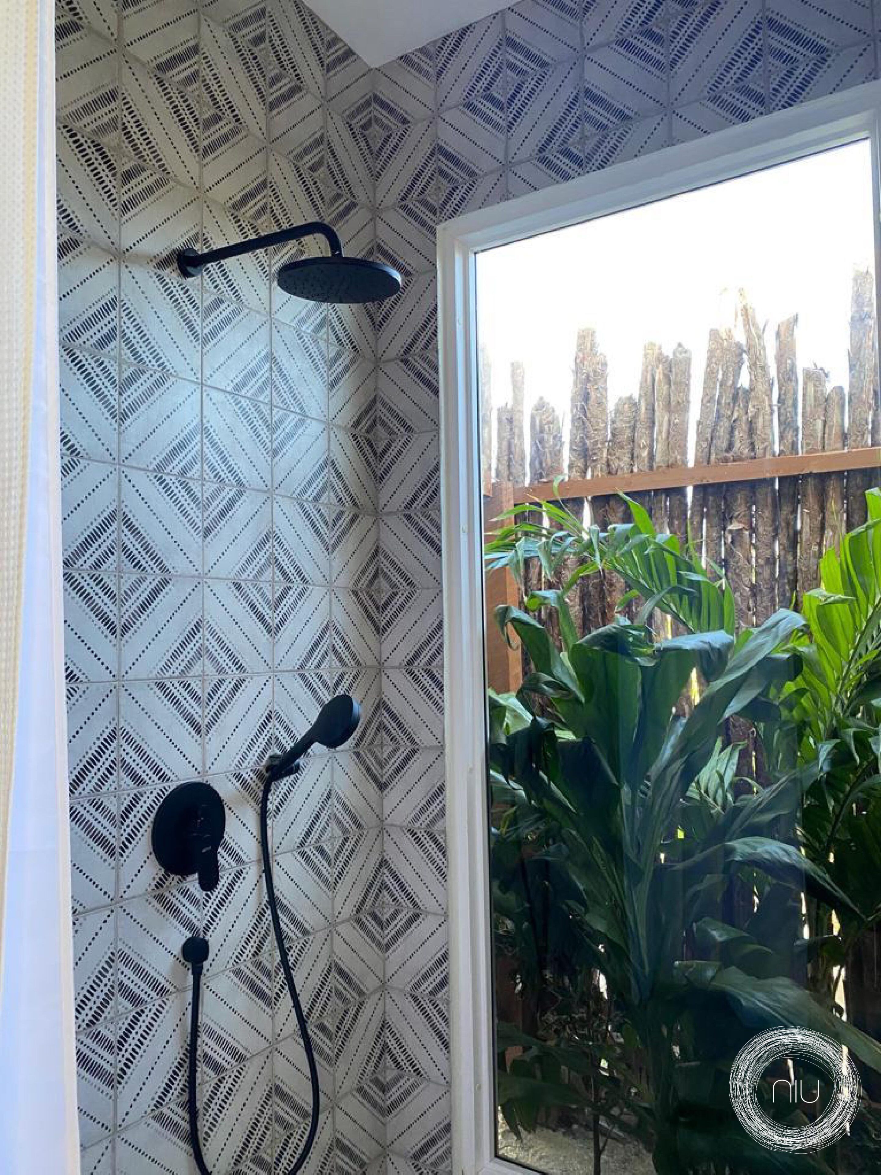 A bathroom with patterned tiles, a shower, and a view of a wooden fence and plants.