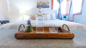 Una bandeja de madera con una botella, un vaso y una pequeña planta sobre la cama.