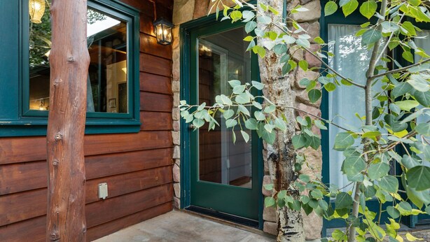 Fachada de madera con un muro de piedra, una puerta verde y una ventana con un accesorio de iluminación.