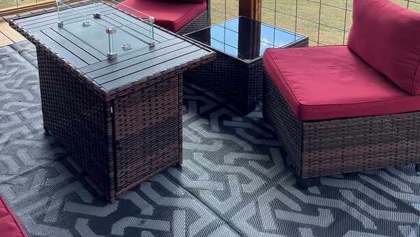 A covered patio with wicker furniture, a glass table, and a view of a mountainous landscape.