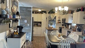 A spacious kitchen with white cabinetry, a dining area with a wooden table and white chairs, and a cozy seating area with a brown sofa.