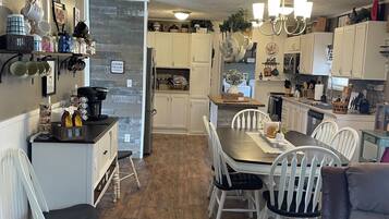 A spacious kitchen with white cabinetry, a dining area with a wooden table and white chairs, and a cozy seating area with a brown sofa.