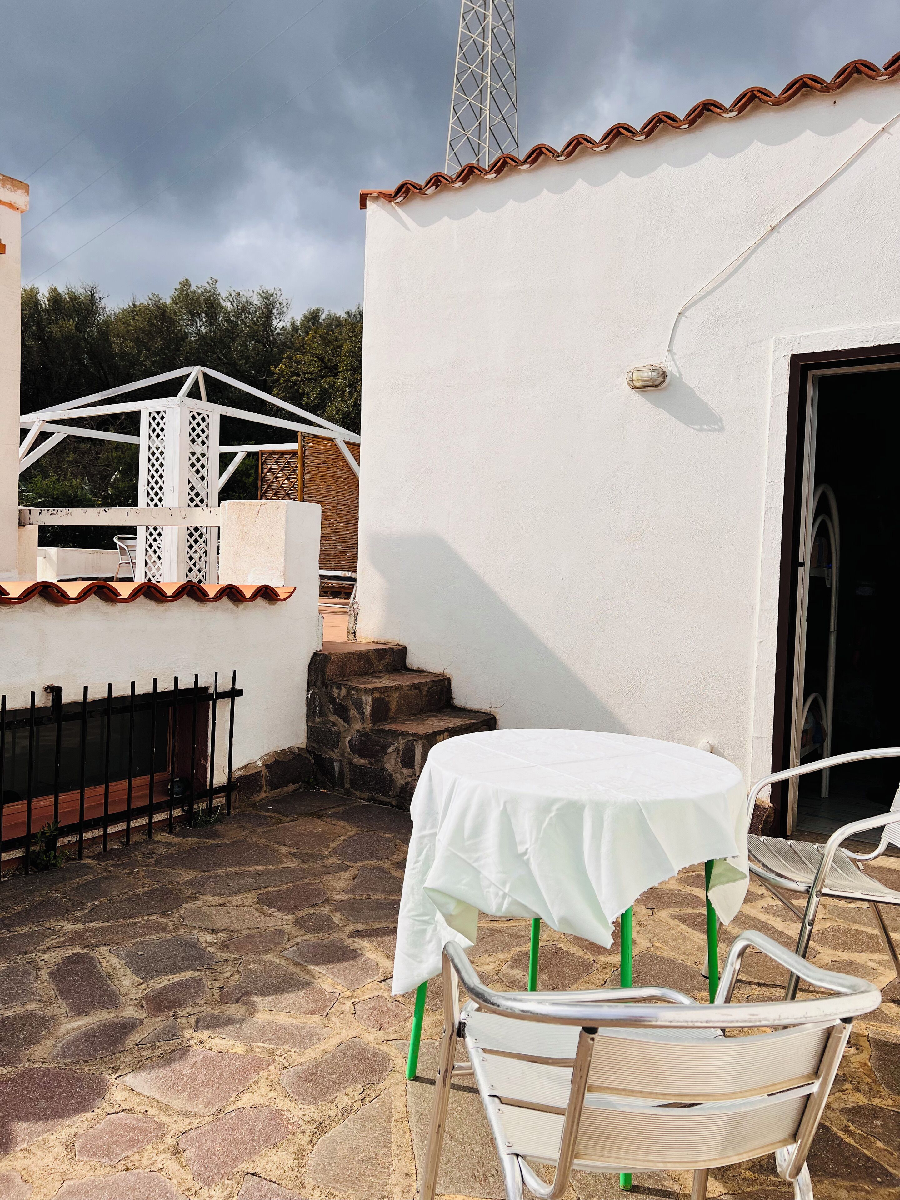 A patio area with a table and chairs, a white wall, a metal fence, and a staircase.