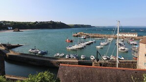 A harbor with boats docked, a stone building, and a view of the coastline. - Sea Haze (Tenby)