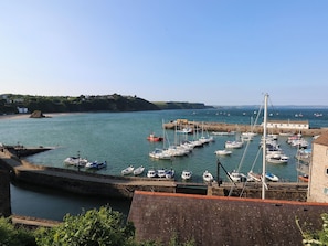 A harbor with boats docked, a stone building, and a view of the coastline. - Sea Haze (Tenby)