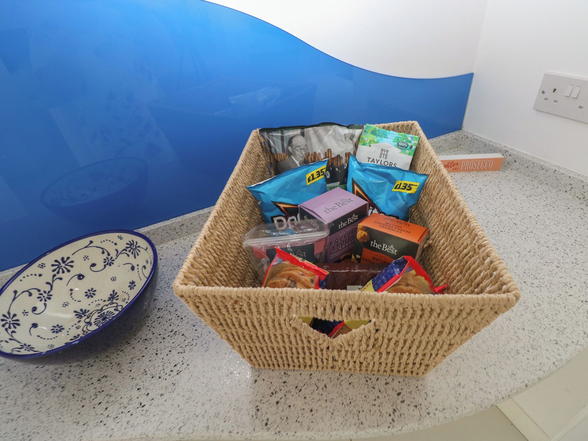 A wicker basket filled with snacks and a bowl on a kitchen counter.