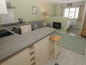 Une cuisine compacte dotée d’appareils électroménagers modernes, un canapé gris, un petit tabouret en bois et une cheminée.