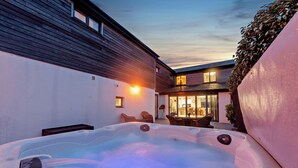 A hot tub in a backyard with a wooden house and a glass door leading to a dining area. - Sea Haze (Tenby)