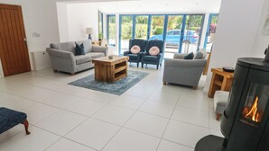 A living room with a fireplace, two sofas, a coffee table, and a large window with a view of parked cars. - Sea Haze (Tenby)