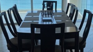 A dining area with a table and chairs, large windows with a view of the sea, and a glass railing.