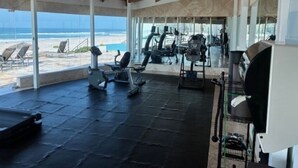 A gym with exercise equipment and a view of the beach.