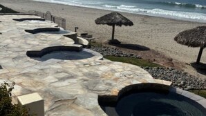 A stone pool area with a view of the ocean, surrounded by a stone deck and thatched umbrellas.