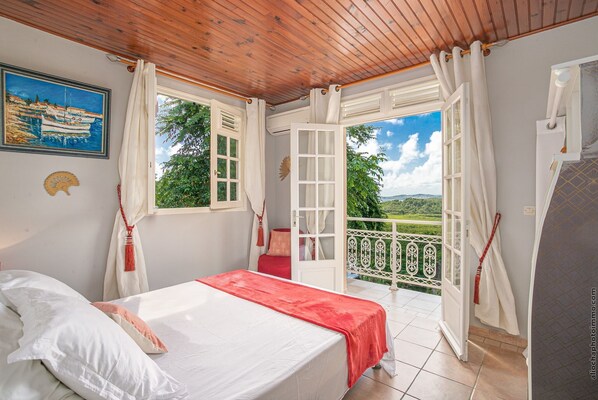 Un dormitorio con cama, una ventana con cortinas, vistas al exterior y un cuadro en la pared.