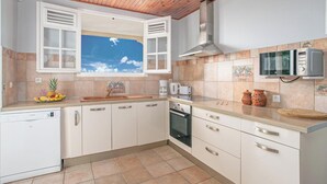 A kitchen with white cabinets, a wooden ceiling, a window with open shutters, a microwave, and a dishwasher. - Villa panoramic sea view & private pool (Le Robert)