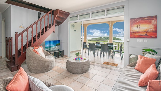 A spacious living area with a wooden staircase, wicker furniture, a round coffee table, and a view of the outdoors. - Villa panoramic sea view & private pool (Le Robert)