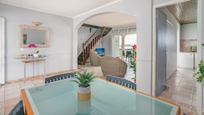 A spacious living area with a glass-top dining table, a staircase, and a kitchen visible through an archway. - Villa panoramic sea view & private pool (Le Robert)