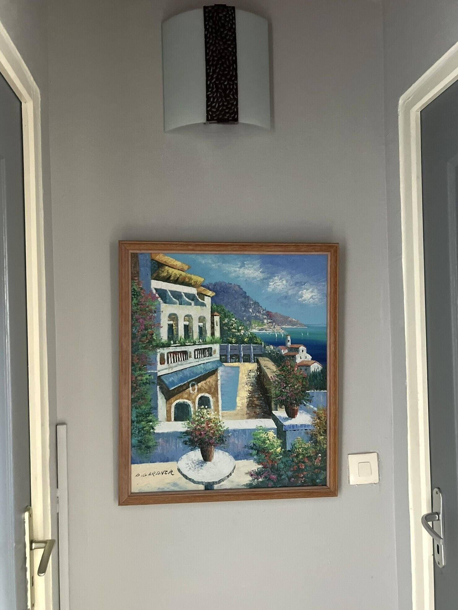 Ein Gemälde einer Küstenstadt mit Gebäuden und Meerblick, gerahmt und an einer Wand aufgehängt.