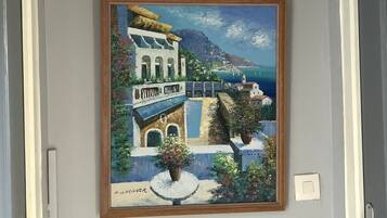 Ein Gemälde einer Küstenstadt mit Gebäuden und Meerblick, gerahmt und an einer Wand aufgehängt.