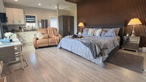 Una camera da letto moderna con un letto grande, comodini, un divano e un angolo cottura sullo sfondo.
