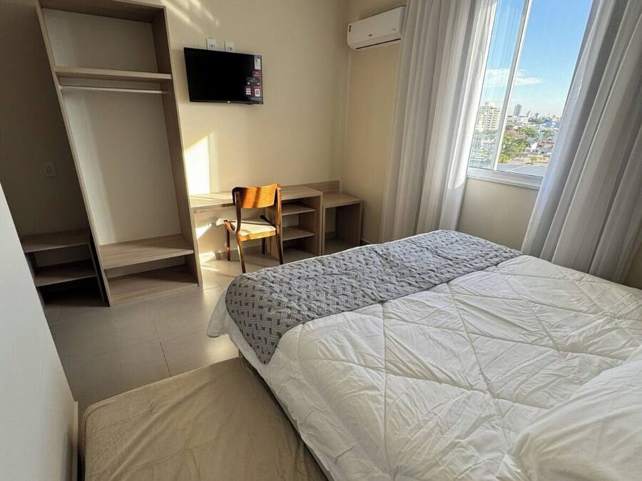 A hotel room with a bed, a desk, a chair, a TV, and a window with curtains.
