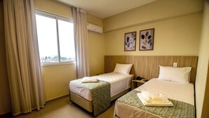 A hotel room with two beds, a window with curtains, an air conditioner, and two framed pictures on the wall. - MLG HOTEL (Mogi das Cruzes)
