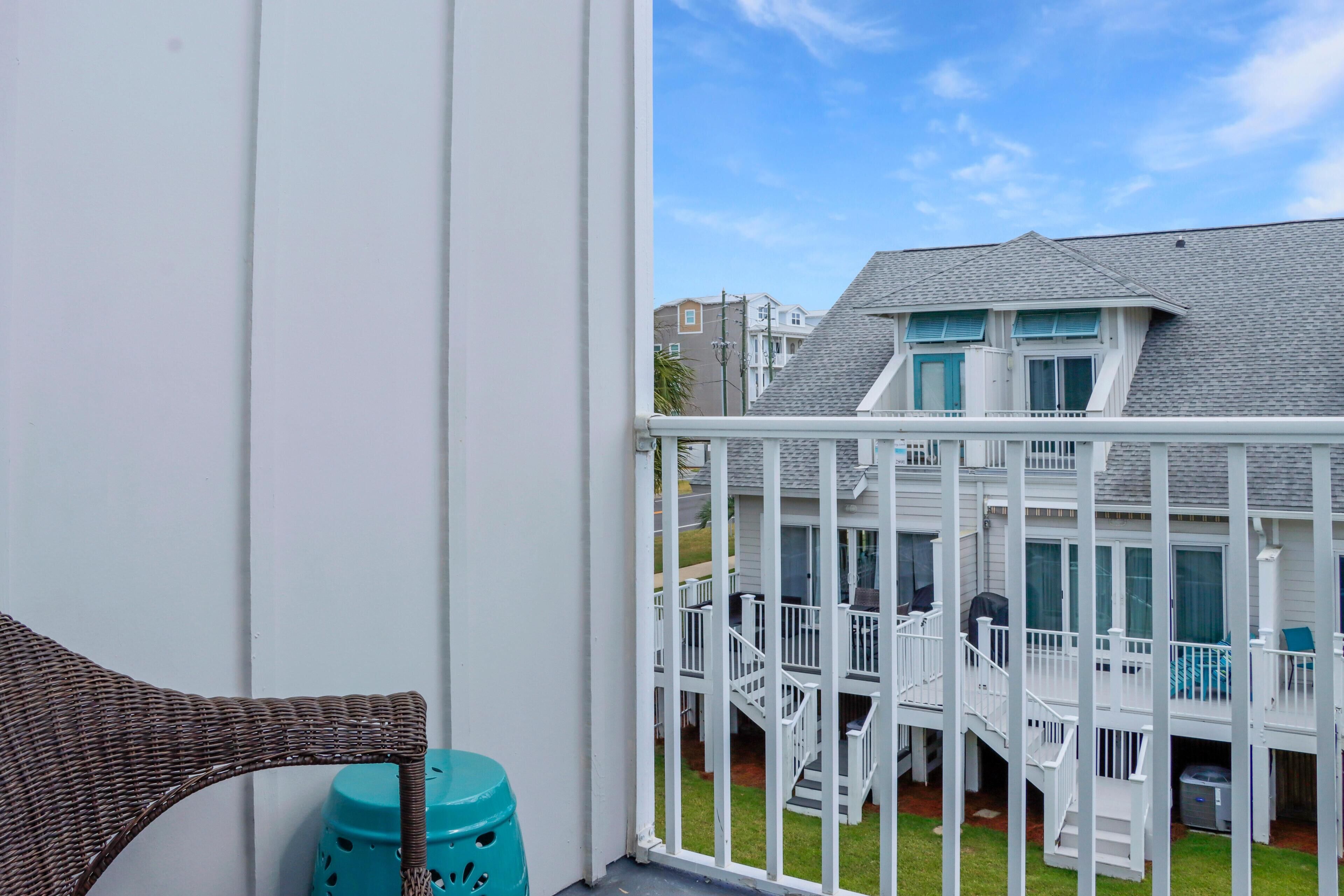 A balcony with a wicker chair and a blue stool.