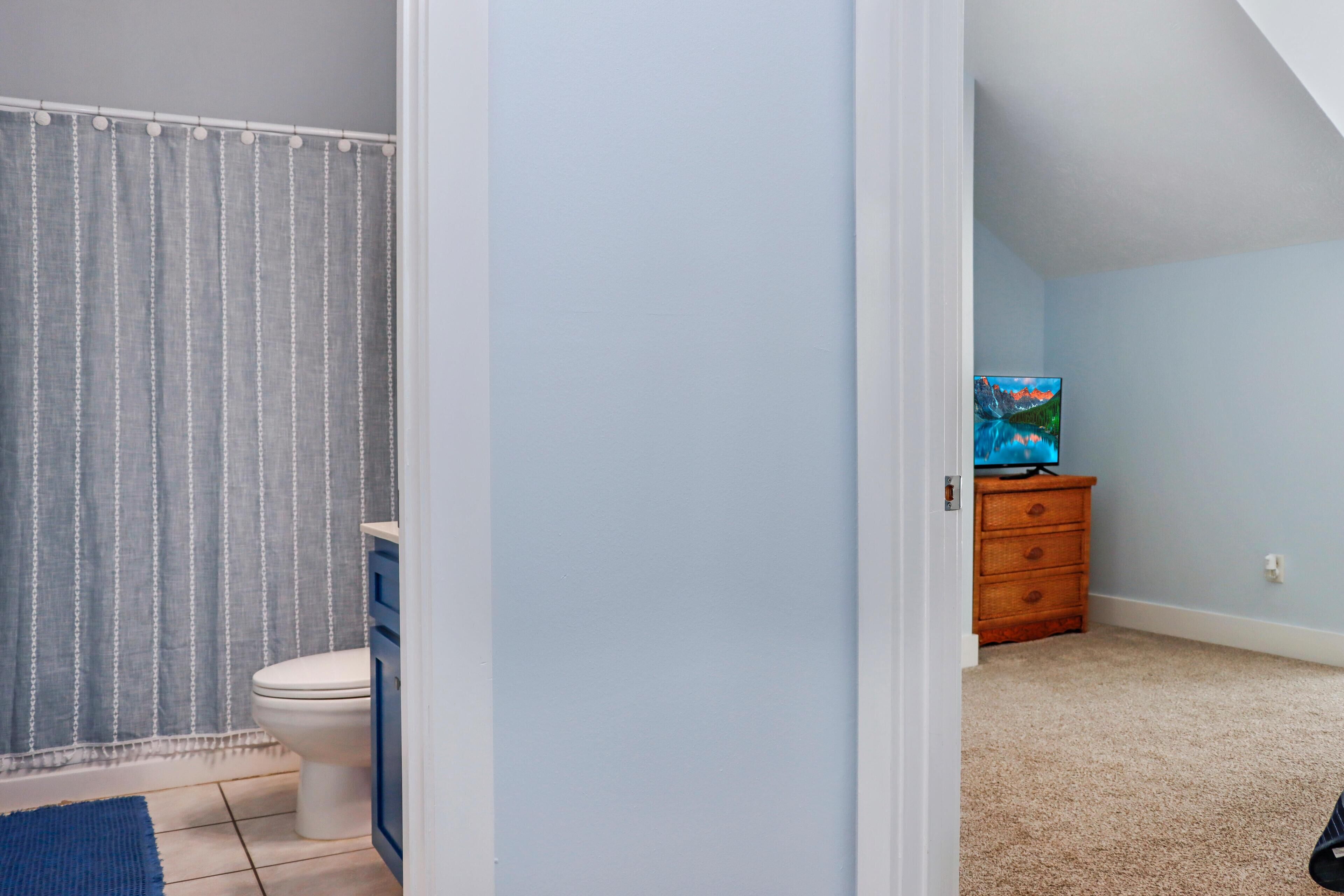 A bathroom with a toilet, a shower curtain, and a blue rug.