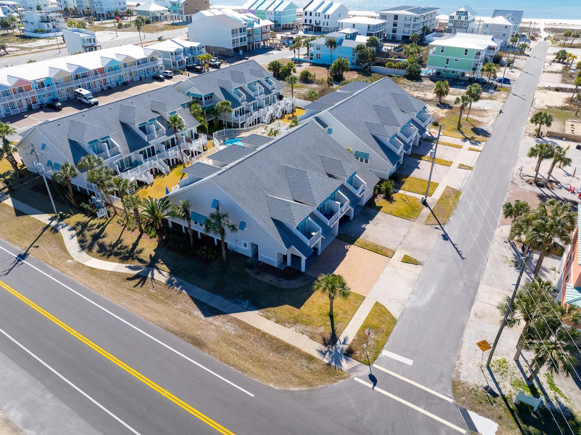 A coastal hotel with multiple-story buildings, a parking lot, and a beach view.