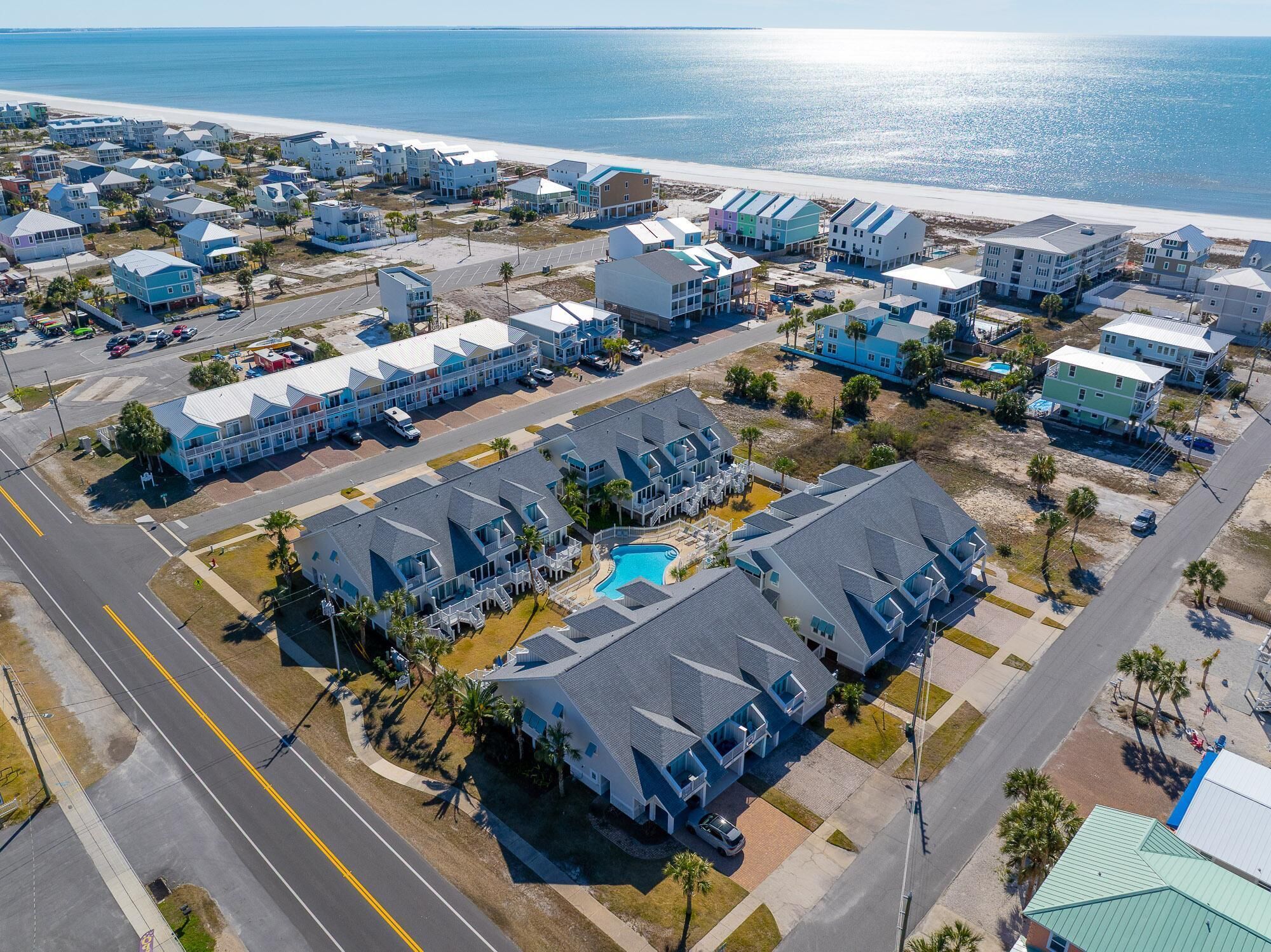 Vista aérea de un complejo hotelero frente al mar, con varias construcciones, una piscina y una playa al fondo.