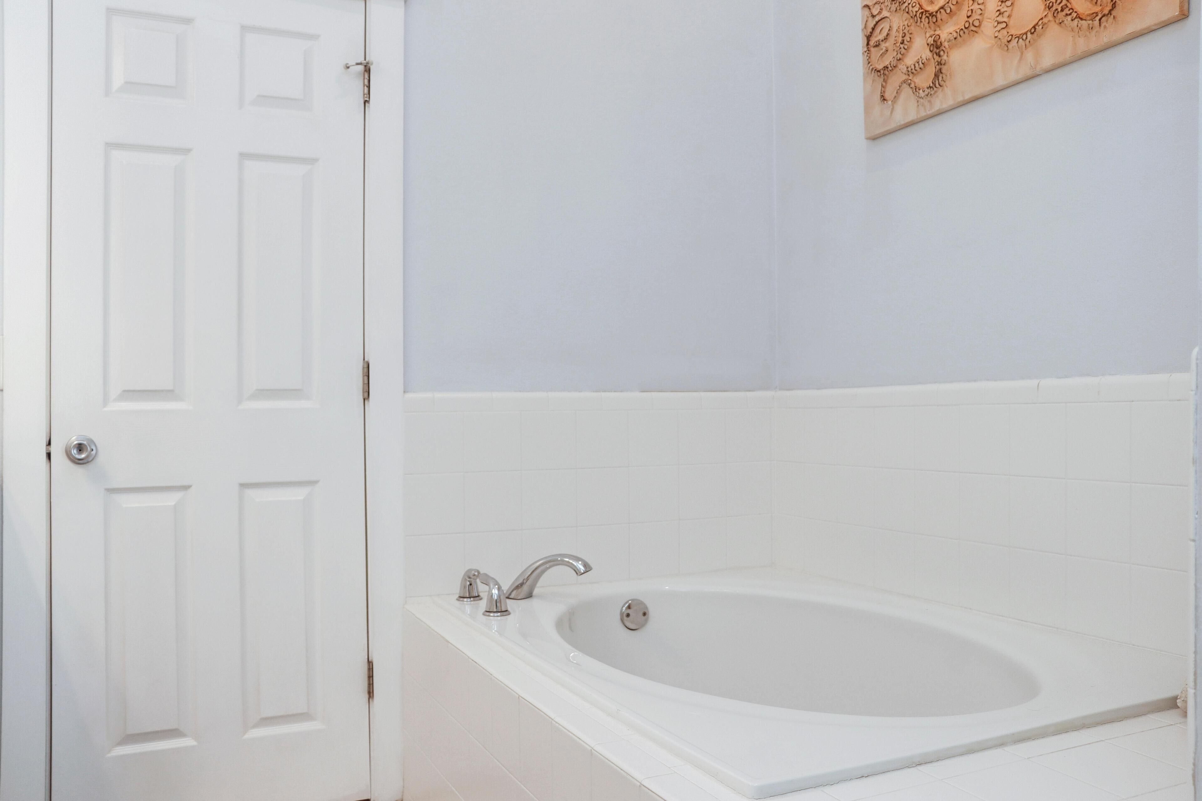 A bathroom with a white bathtub, a door, and a wall-mounted artwork.