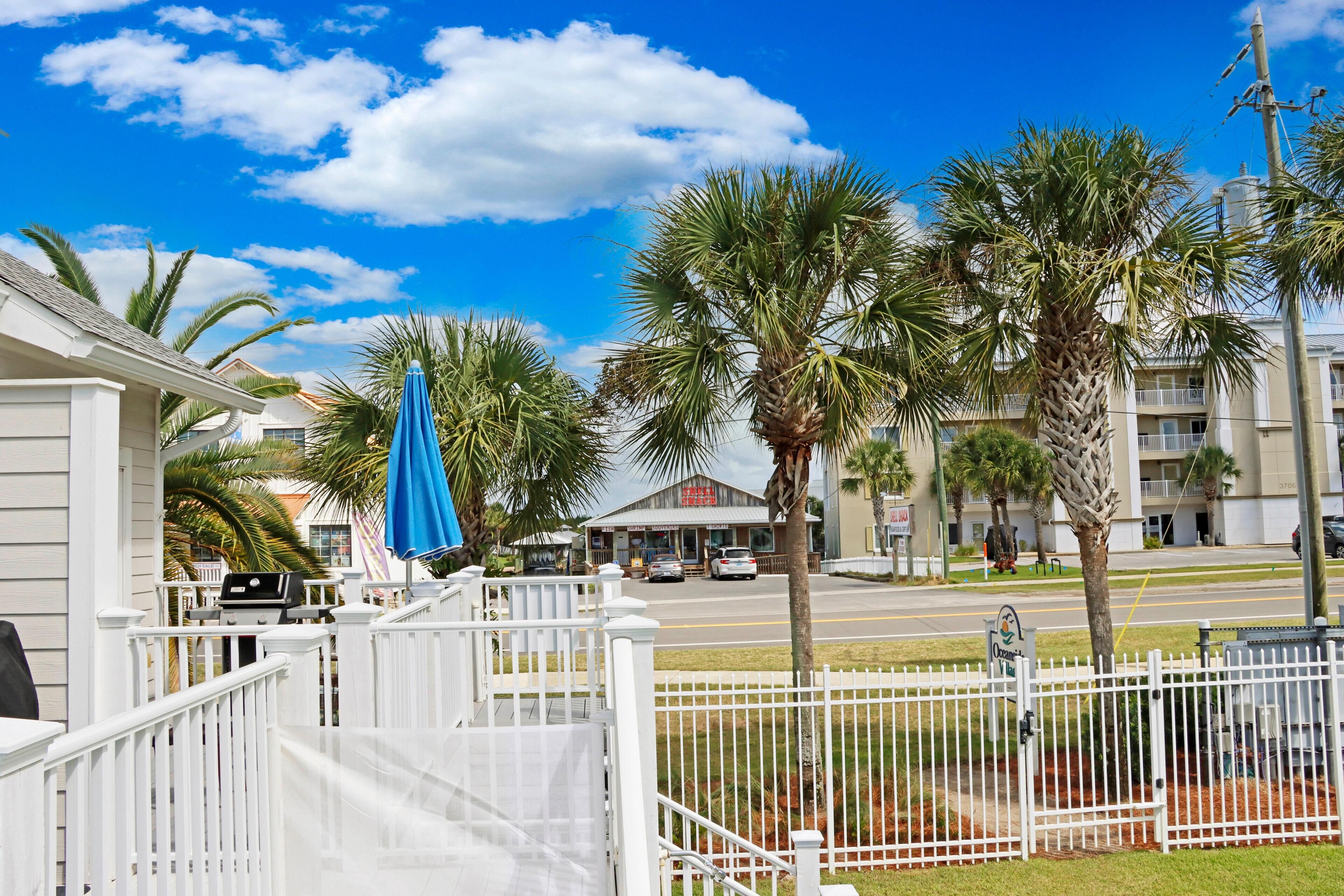 A beachfront property with a white fence, a blue umbrella, and palm trees.
