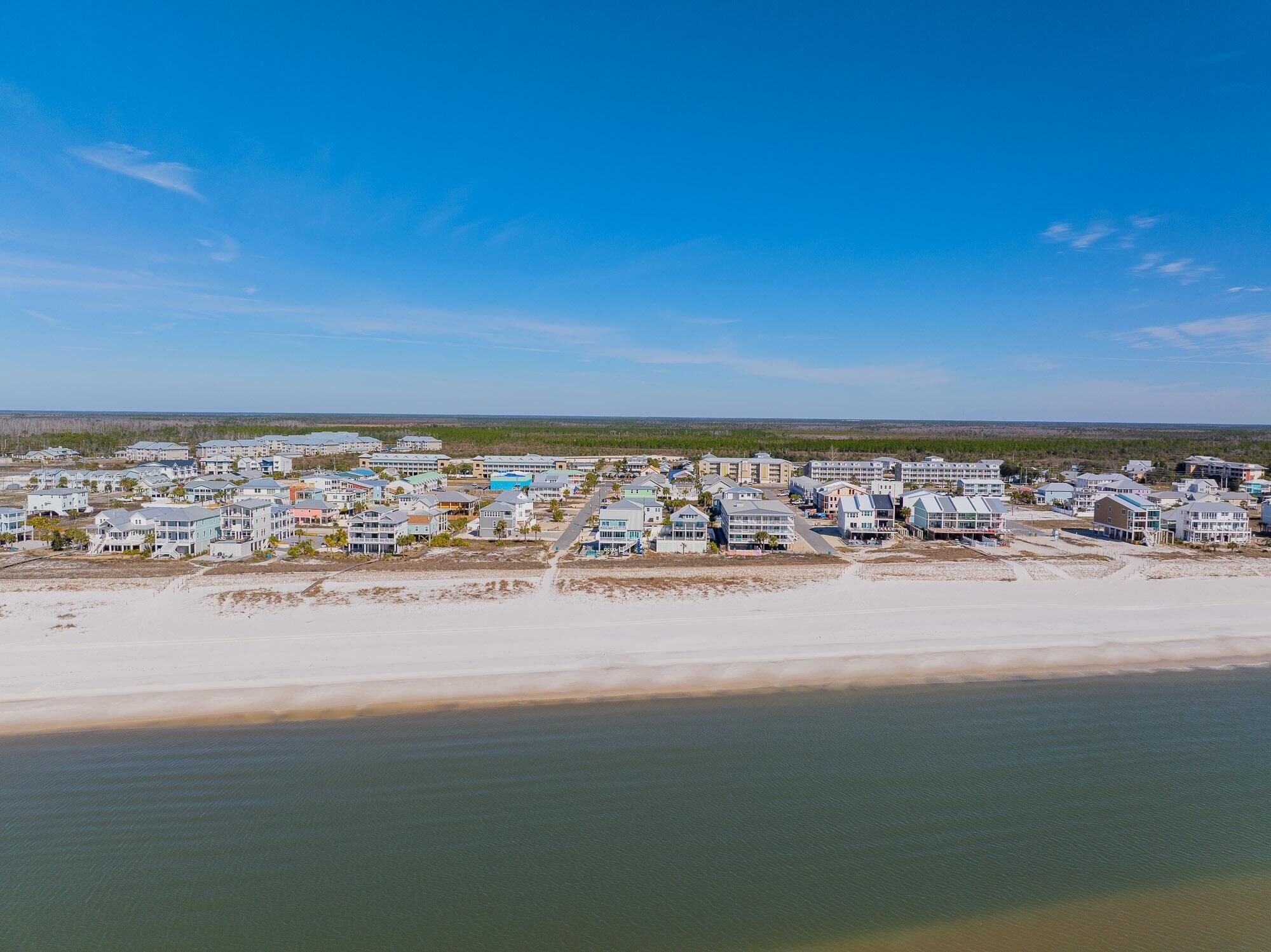 An aerial view of a coastal resort with multiple buildings, beachfront access, and a clear sky.