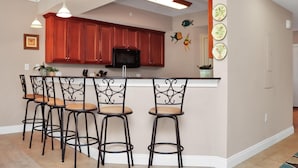 A kitchen with a central island, bar stools, a microwave, and decorative wall art. - Paradise Shores 105 (Port St. Joe)