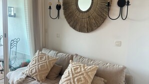 Un canapé beige agrémenté de coussins à motifs, un miroir rond et des appliques murales avec des ampoules.